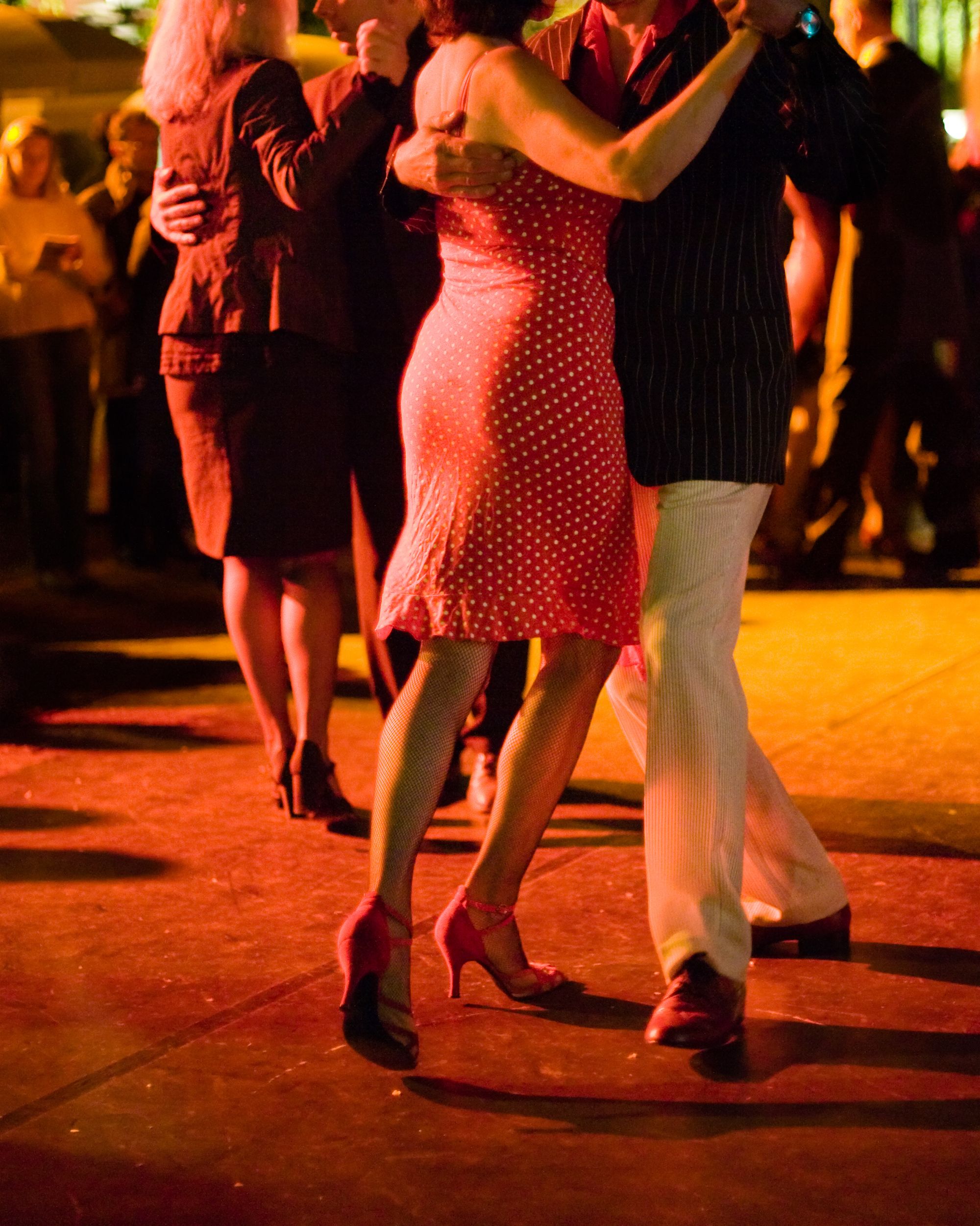 open air milonga at night people dancing argentine tango outdoors, focus on legs of the front couple heads are not in frame natural light, high iso