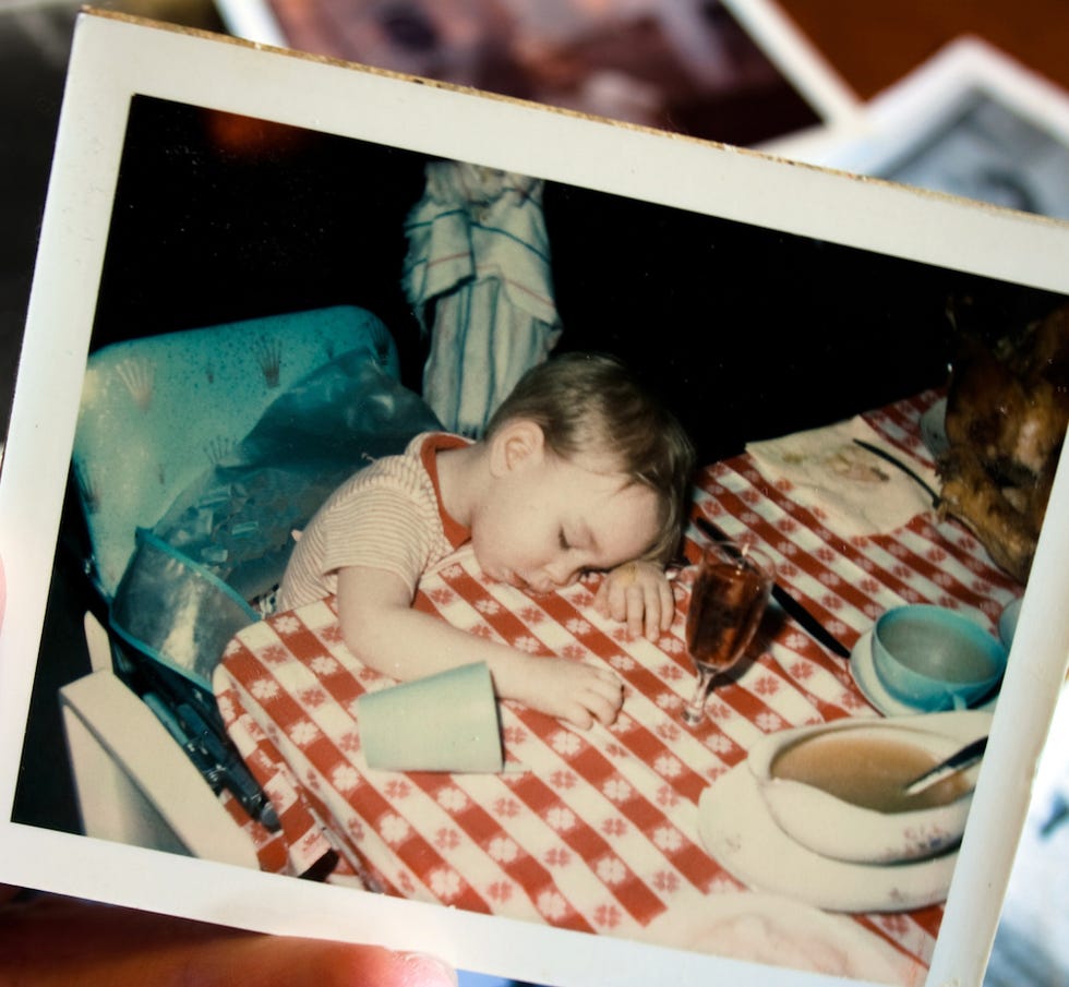 an old photo of a baby sleeping in a high chair next to a red and white checked tablecloth