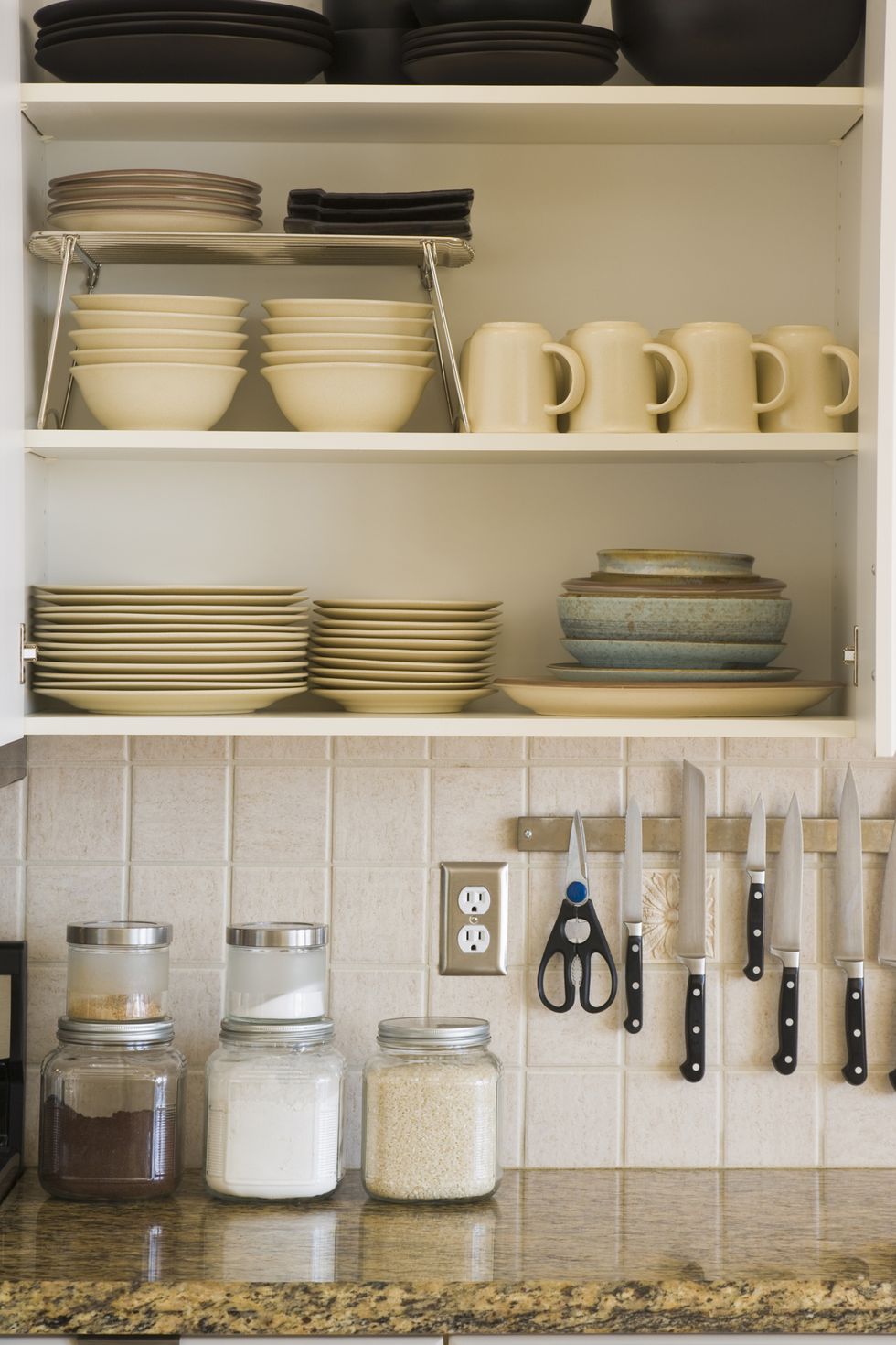 kitchen counter top with open cupboard with stacks of dishes, bowls and cups