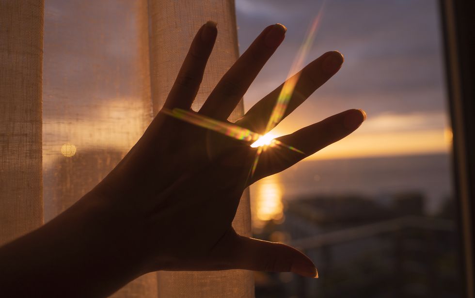 sunset sunbeams through fingers of female hand in evening