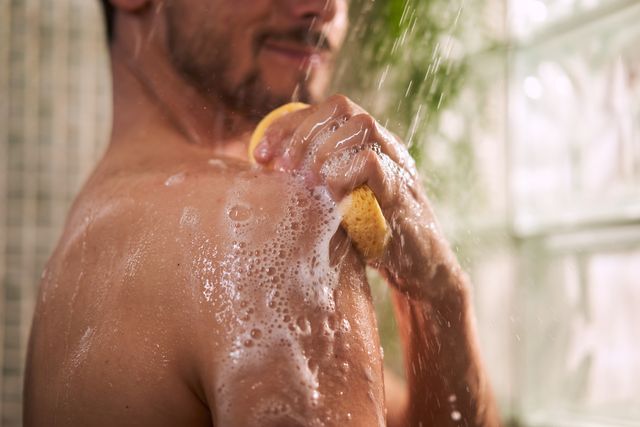 close up of unrecognizable man taking a shower, using sponge to rub his shoulder copy space