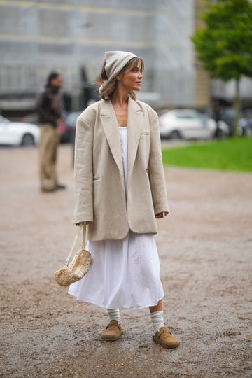 copenhagen, denmark august 09 a guest wears a beige silk scarf as a headband, a white long dress, a beige oversized blazer jacket, a beige and white latte striped print pattern braided wickers handbag, white socks, brown suede mules , outside operasport, during the copenhagen fashion week springsummer 2024 on august 09, 2023 in copenhagen, denmark photo by edward berthelotgetty images