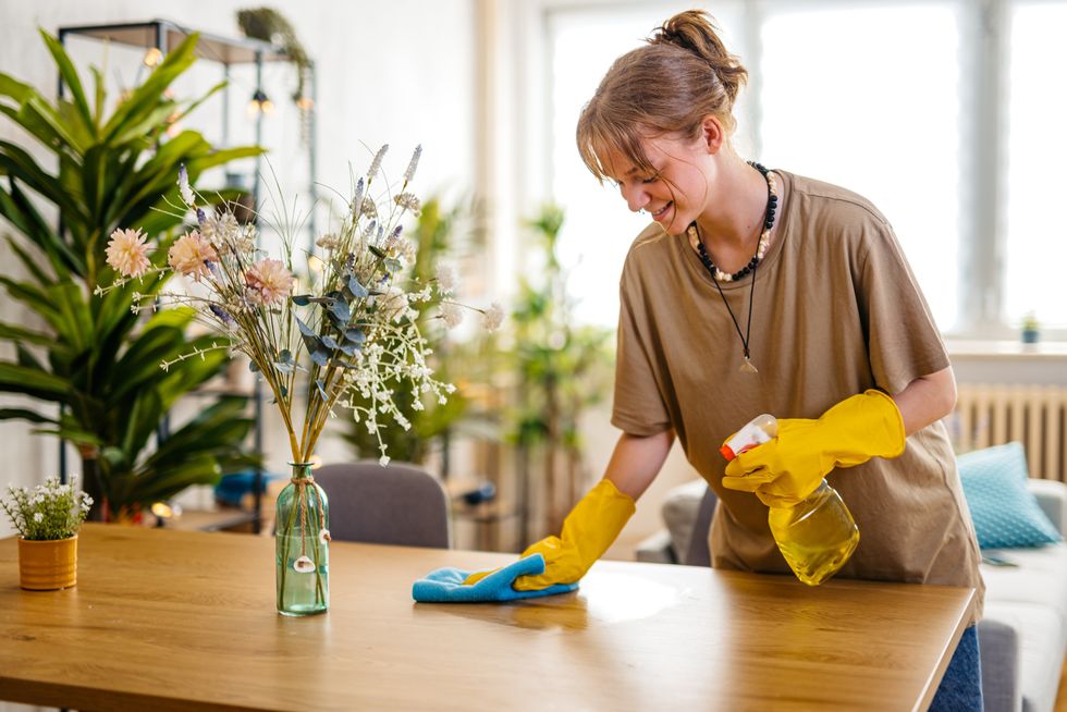 young smiling woman wiping the dining table surface using a cloth and a spray bottle