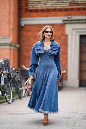 copenhagen, denmark august 10 a guest wears black sunglasses, a gold chain necklace, a blue denim micro cropped jacket, a blue denim embossed striped pattern shoulder off long ripped dress, a brown shiny leather braided leather jodie handbag from bottega veneta, camel shiny leather varnished platform high heels shoes from chanel , outside mark kenly domino tan, during the copenhagen fashion week springsummer 2024 on august 10, 2023 in copenhagen, denmark photo by edward berthelotgetty images