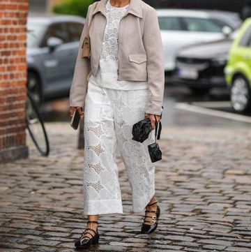 copenhagen, denmark august 09 a guest wears silver earrings, a beige denim zipper jacket, a brown matte suede shoulder bag, a white cut out flower pattern blouse, matching white cut out flower pattern wide legs pants, a black umbrella, a black camera from canon, black shiny varnished leather belted ballerinas , outside paolina russo, during the copenhagen fashion week springsummer 2024 on august 09, 2023 in copenhagen, denmark photo by edward berthelotgetty images