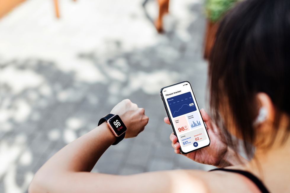 over the shoulder view of young woman using running app on smart watch and smartphone to track pace and time doing exercise with wearable technology mockup image for young woman using smartphone and smart watch