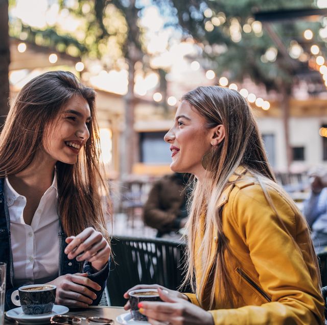 female friends sitting in a cafe garden, drinking coffee, gossiping and smiling