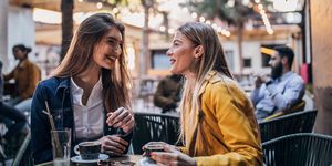 female friends sitting in a cafe garden, drinking coffee, gossiping and smiling