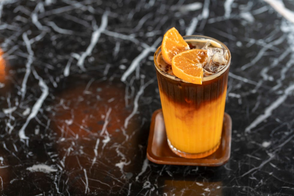 americano coffee mixed with orange juice in clear glass placed on a wooden tray on a black marble cut white table