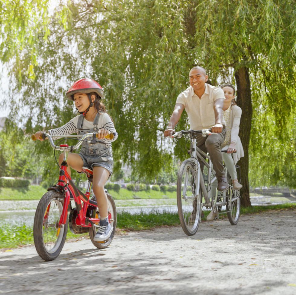 smiling family riding bicycle together on footpath by lake in public park