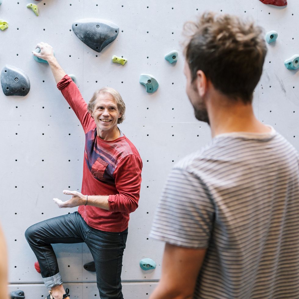 smiling mature instructor teaching male and female students about bouldering in gym
