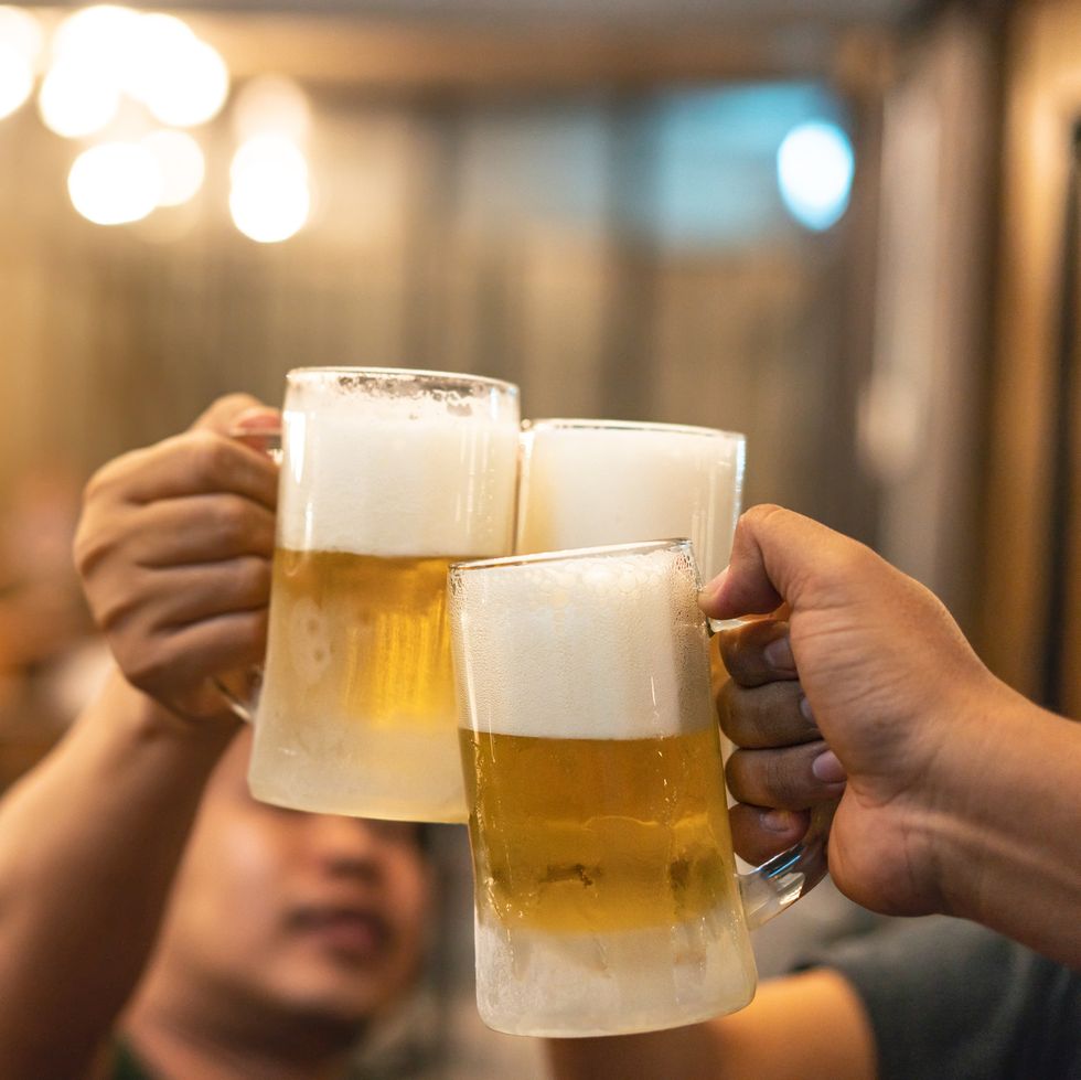 beer glasses raised in a toast close up hands with glasses blurred bar interior at the background