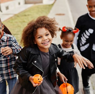 group of smiling kids trick or treating outdoors and walking to camera holding pails