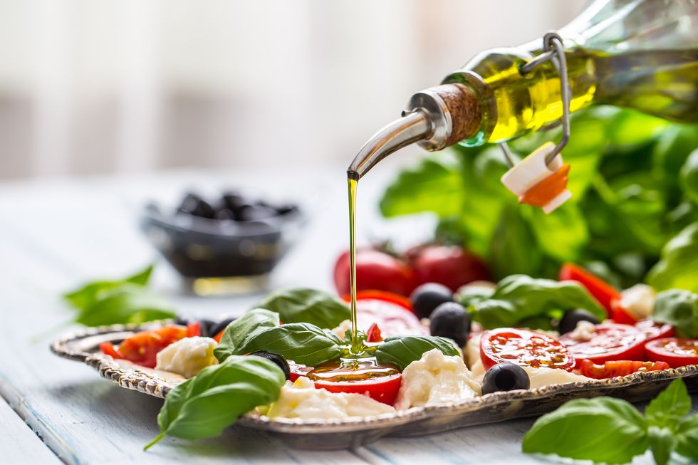 pouring olive oil on caprese salad healthy italian or mediterranean meal