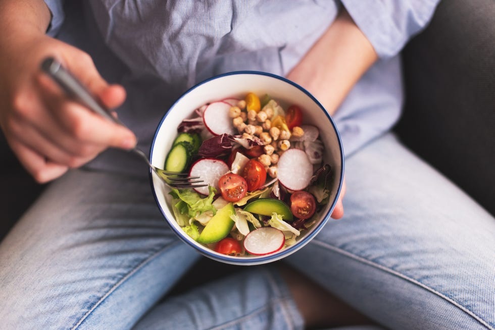 green vegan breakfast meal in bowl with spinach, arugula, avocado, seeds and sprouts girl in leggins holding plate with hands visible, top view clean eating, dieting, vegan food concept