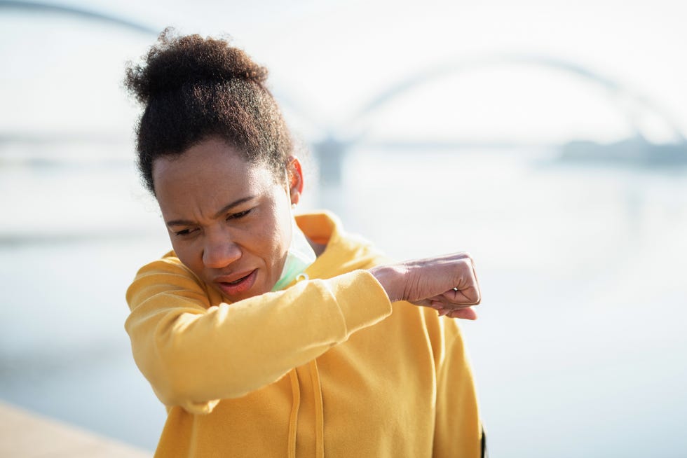 african american mid adult woman coughing while exercising outdoors wearing protective mask and showing symptoms of corona virus