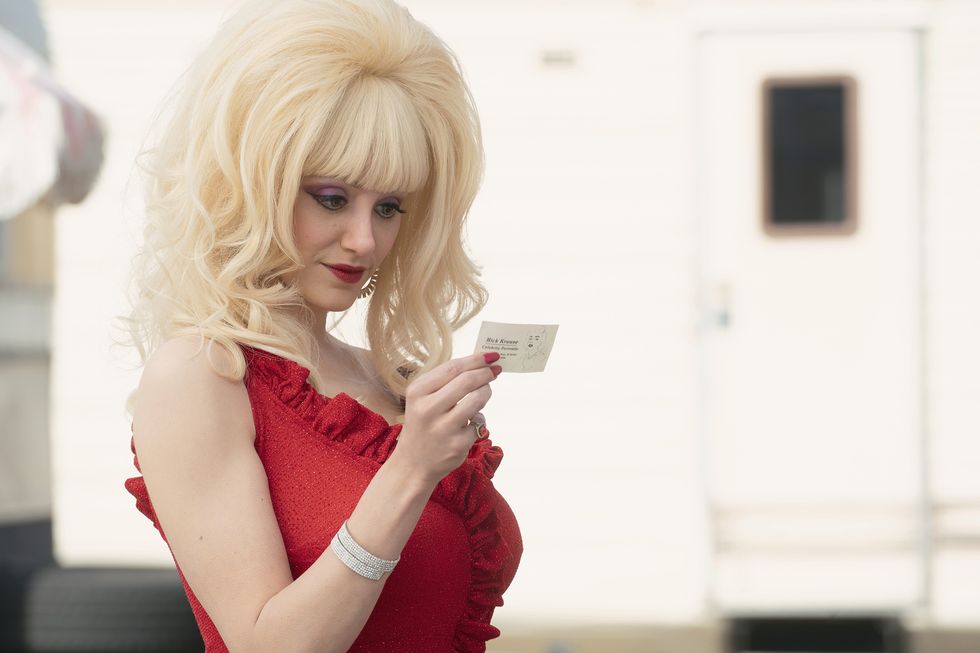 actress emmy rossum wearing prosthetic breasts and a huge blond wig in a red dress for her role as la pop icon angelyne
