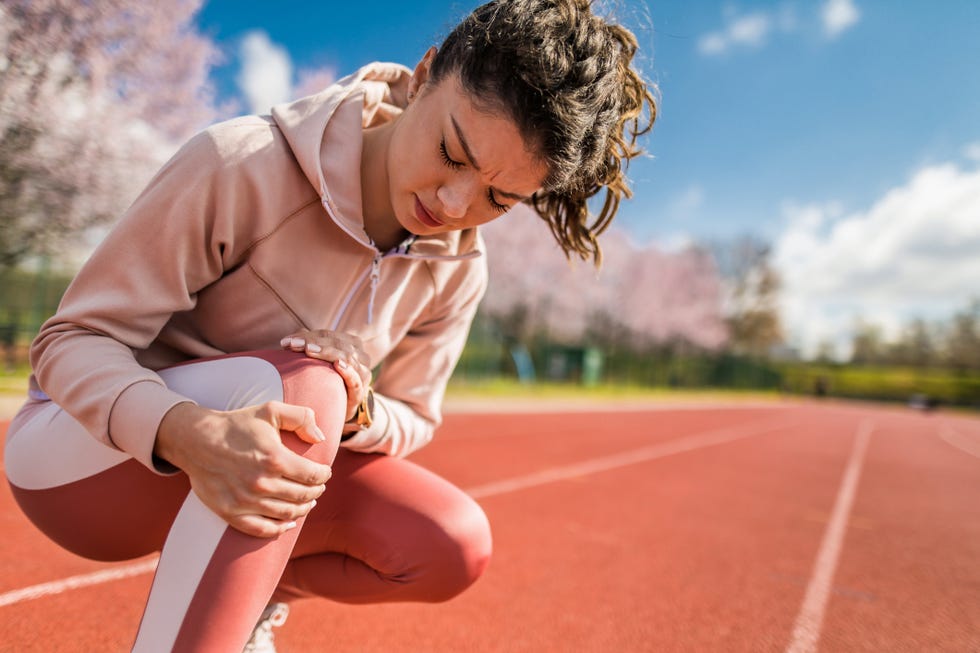 young female athlete having knee pain she injured her knee while running on sports track