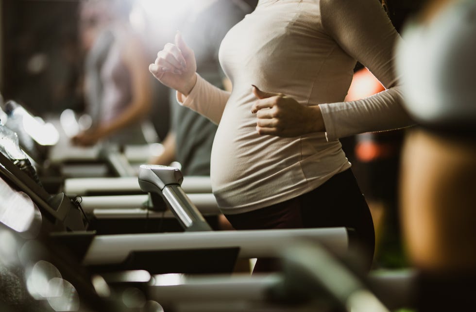 unrecognizable pregnant woman jogging during sports training on treadmill in a gym