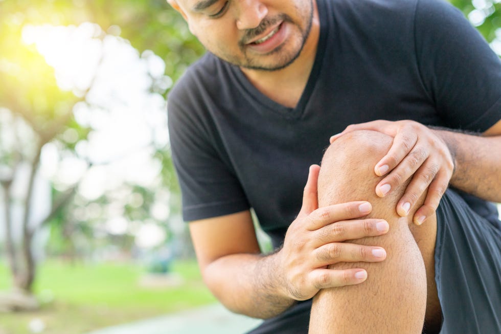 a young male in sports outfits black injured his knee during exercise in the park low section of sports man suffering from joint pain while sitting on track during accident from exercise concept