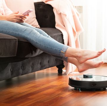 low section of woman sitting on sofa with robotic vacuum cleaner at home