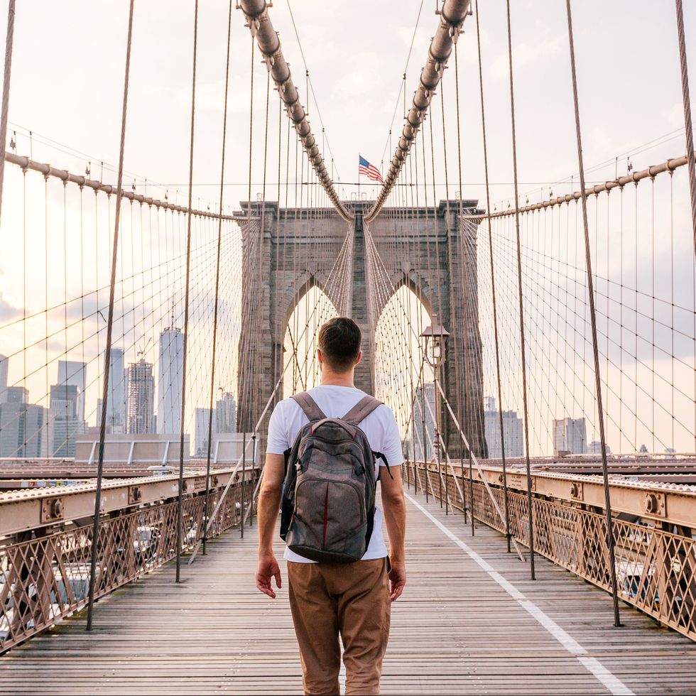 rear view of a young man with backpack walking on brooklyn bridge, new york city, usa