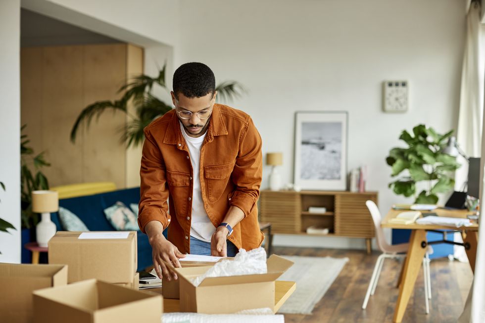 young businessman packing cardboard box at table in apartment male professional is working at home office he is in living room