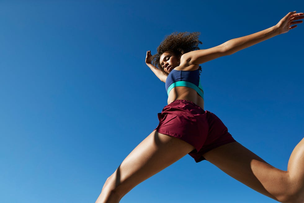 frizzy young female athlete jumping against clear blue sky on sunny day