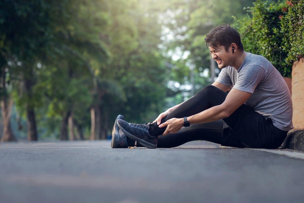 asian man achilles injury on running outdoors man holding achilles tendon by hands close up and suffering with pain sprain ligament or achilles tendonitis