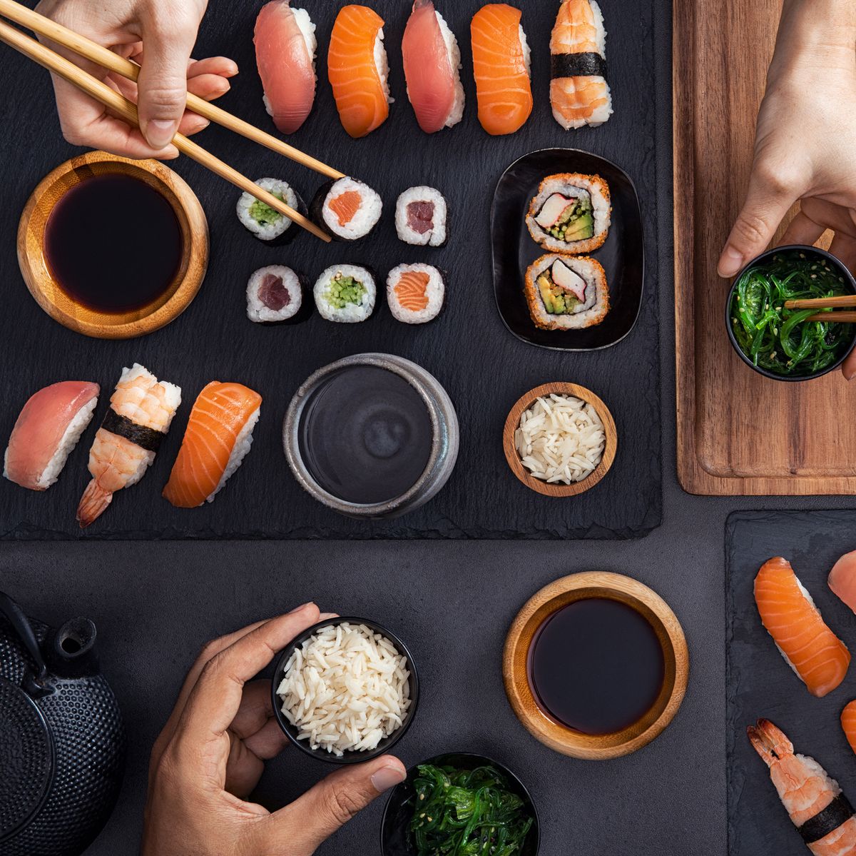 top view of couple hands eating sushi food at japanese restaurant high angle view of woman hand serving seaweed in little bowl with sesame to man while holding hosomaki with chopsticks couple eating and sharing sushi roll, maki, nigiri, uramaki