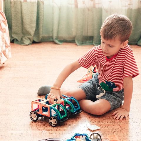 a boy plays with magnetic constructor in children room sitting on cork floor