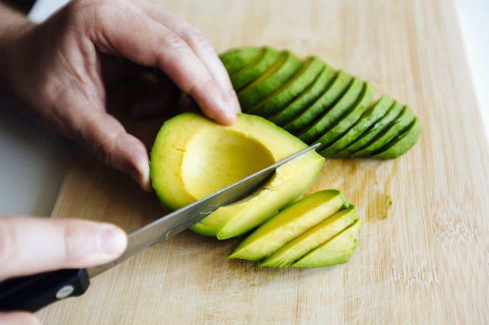 man slicing avocado with a knife on a cutting board close up