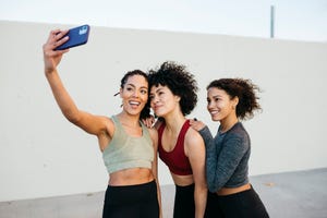 three smiling young women, wearing sports clothes, taking a selfie on an urban scenario, before workout