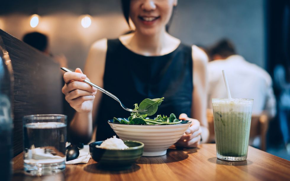 cropped shot of smiling young asian woman eating fresh vegan salad with a glass of green smoothie in a restaurant, enjoying a healthy meal green living healthy eating lifestyle vegetarian and vegan diet concept