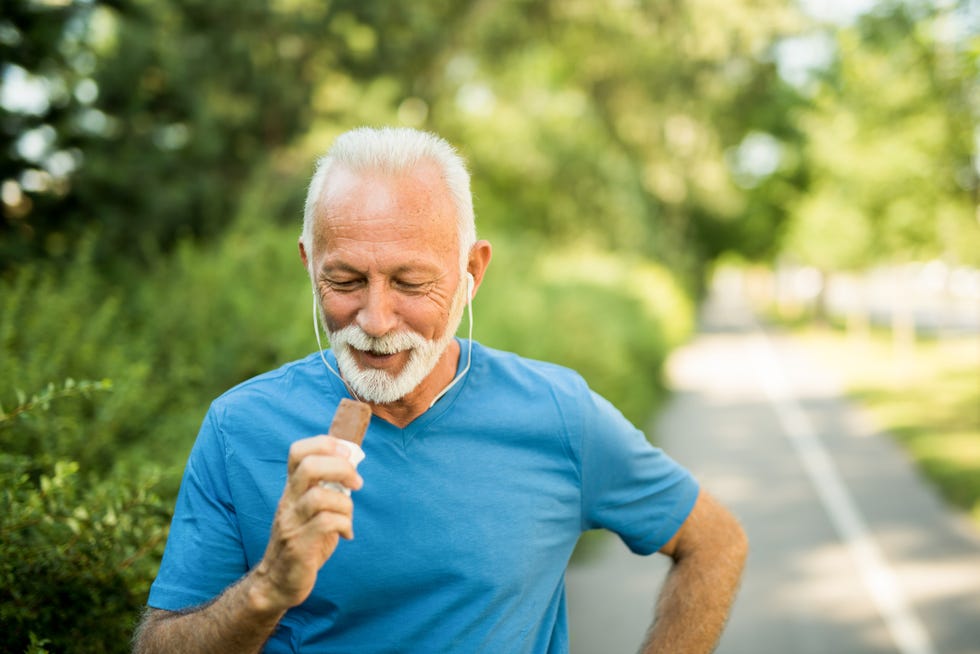 sporty senior man eating a chocolate bar while exercising outdoors