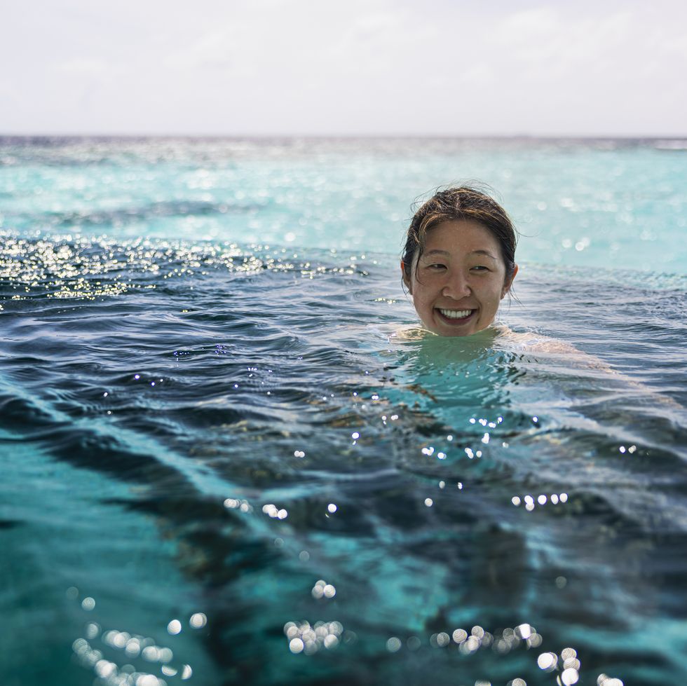 Smiling adult woman mid swimming in infinity pool