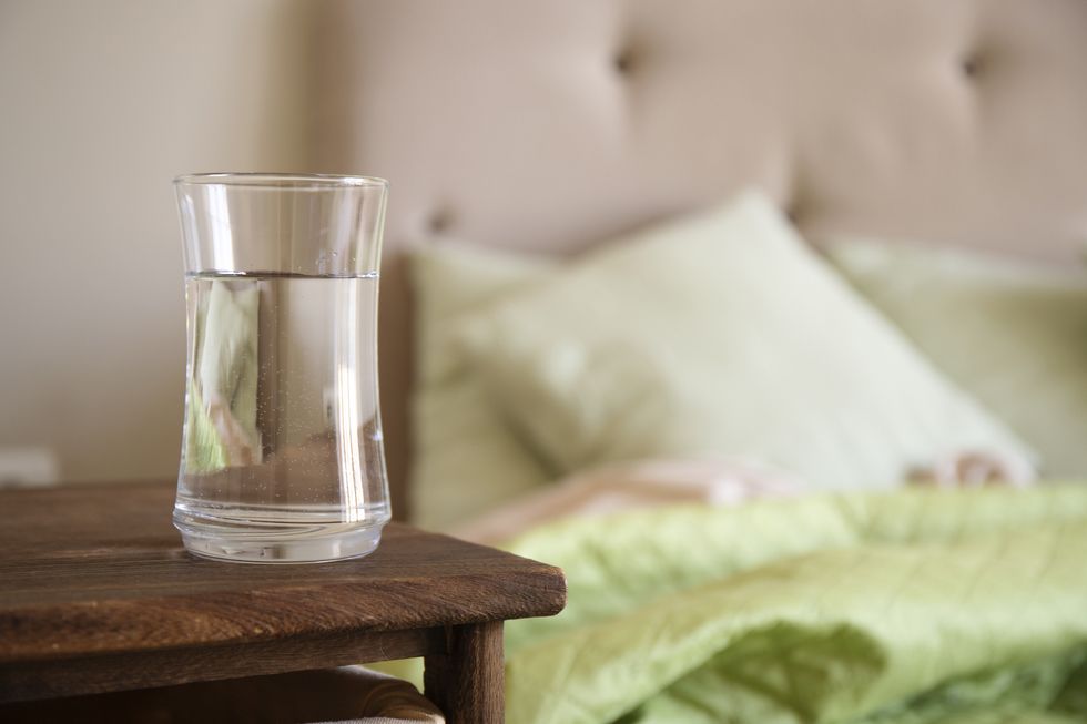 transparent glass with water on a wooden nightstand in bedroom selective focus