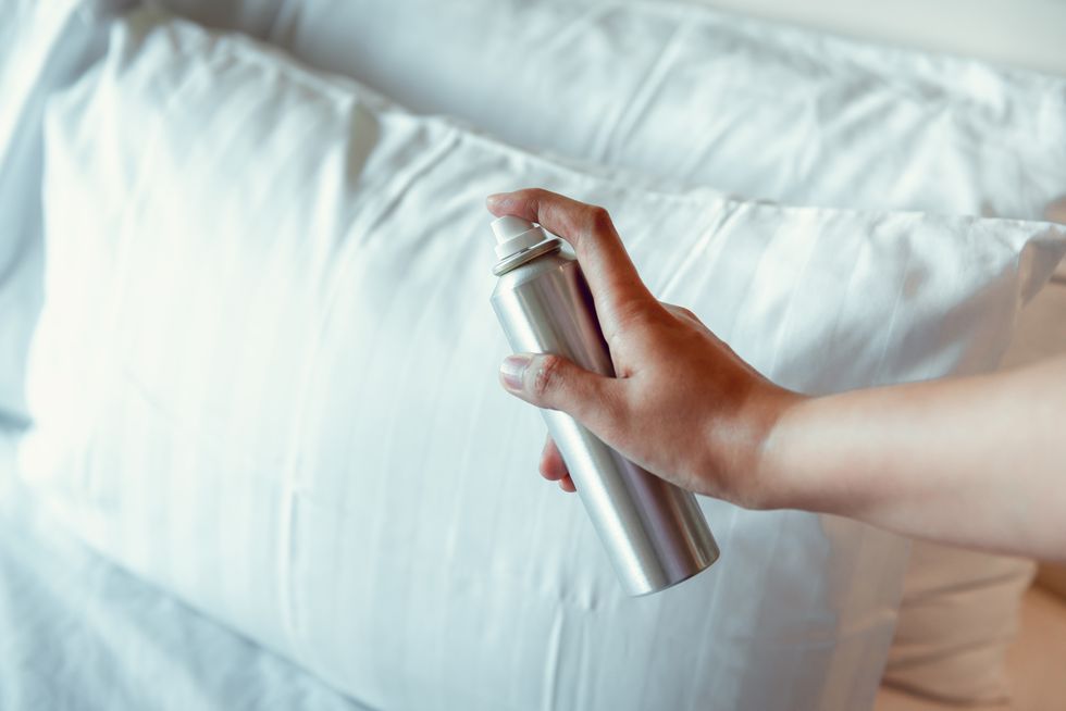 woman hand is spraying air freshener into pillow on bedroom, unpleasant smell and aromatherapy concept
