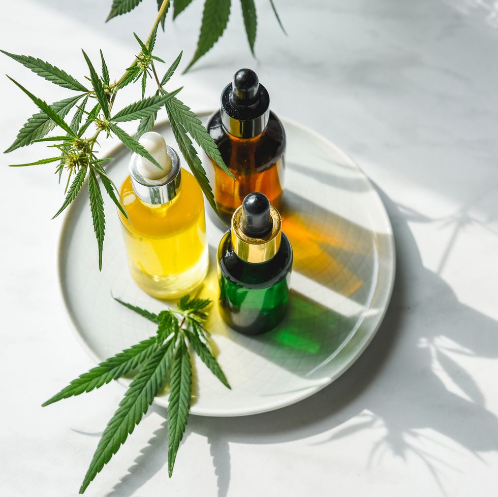 different glass bottles with cbd oil, thc tincture and cannabis leaves on yellow background flat lay, minimalism cosmetics cbd oil