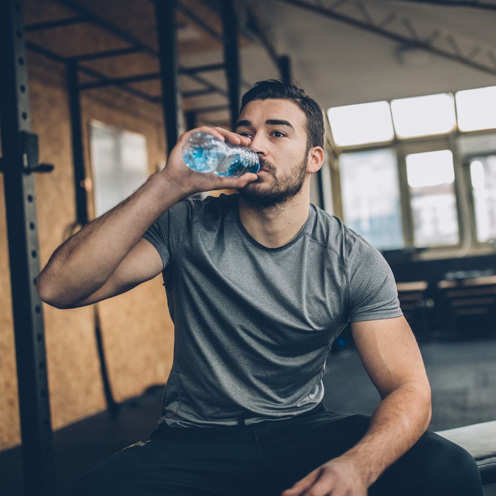 one man, sitting on bench, drinking water after training