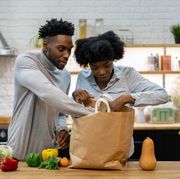 portrait of a happy african american couple at home unpacking the groceries from a shopping bagâ lifestyle concepts