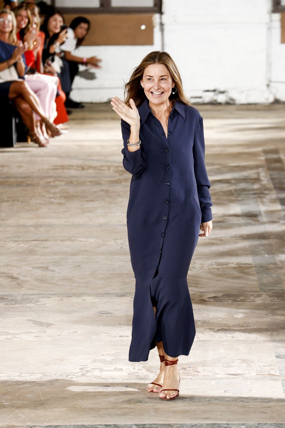 amy ﻿smilovic on the runway after her spring 2019 show wearing a long sleek navy shirt dress and simple brown sandals