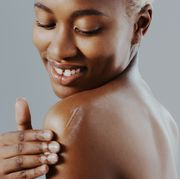 cropped shot of an attractive young woman standing alone and applying lotion to her shoulder against a gray studio background