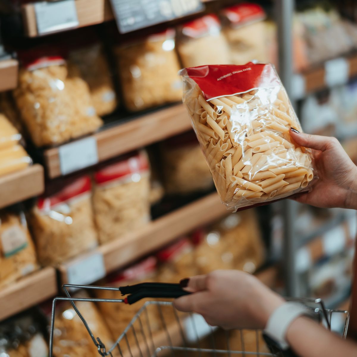 young asian woman carrying a shopping basket, grocery shopping in supermarket, close up of her hand choosing a pack of organic pasta along the aisle healthy eating lifestyle