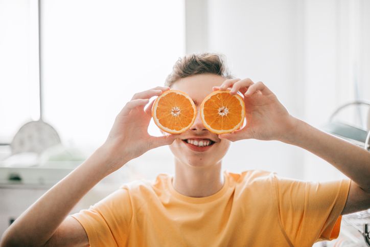 cheerful teenager male holding oranges in front of his eyes at kitchen in the morninghe is confident and happy with backlight