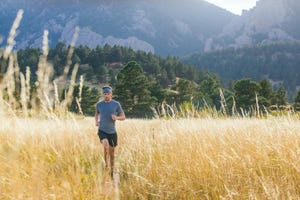 a man runs through tall grass on bear canyon trail above boulder, colorado the flatirons are visible in the background