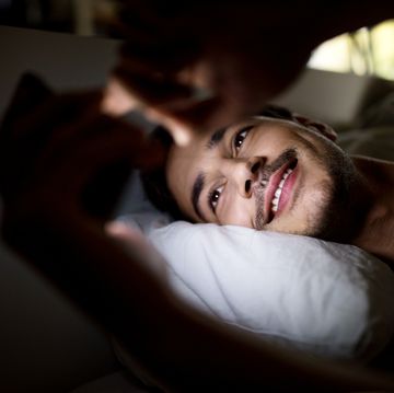 smiling man lying in bed and using his mobile phone