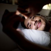 smiling man lying in bed and using his mobile phone