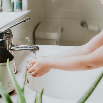 cute little girl washing her hands at a bathroom sink, in a stylish home environment aloe vera plant in foreground and liquid soap and chrome tap featured little girl is confident and content conceptual with space for copy