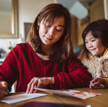 young pretty mom writing greeting card for family with her lovely daughter at home